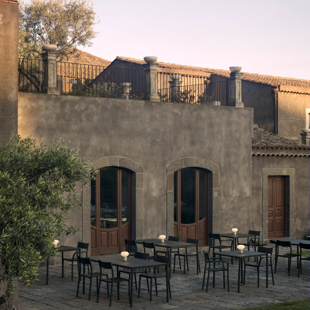 "Elegant outdoor seating with black metal chairs and tables against a rustic stone building backdrop."