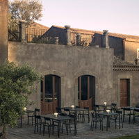 "Elegant outdoor seating with black metal chairs and tables against a rustic stone building backdrop."
