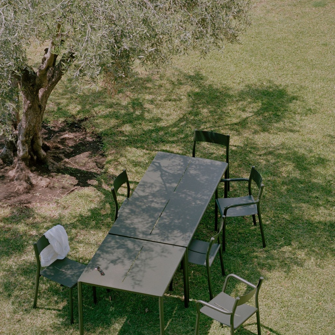 "Elegant green outdoor dining set with sleek black chairs, set in a sunlit garden under a tree's shade."