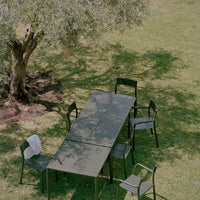"Elegant green outdoor dining set with sleek black chairs, set in a sunlit garden under a tree's shade."