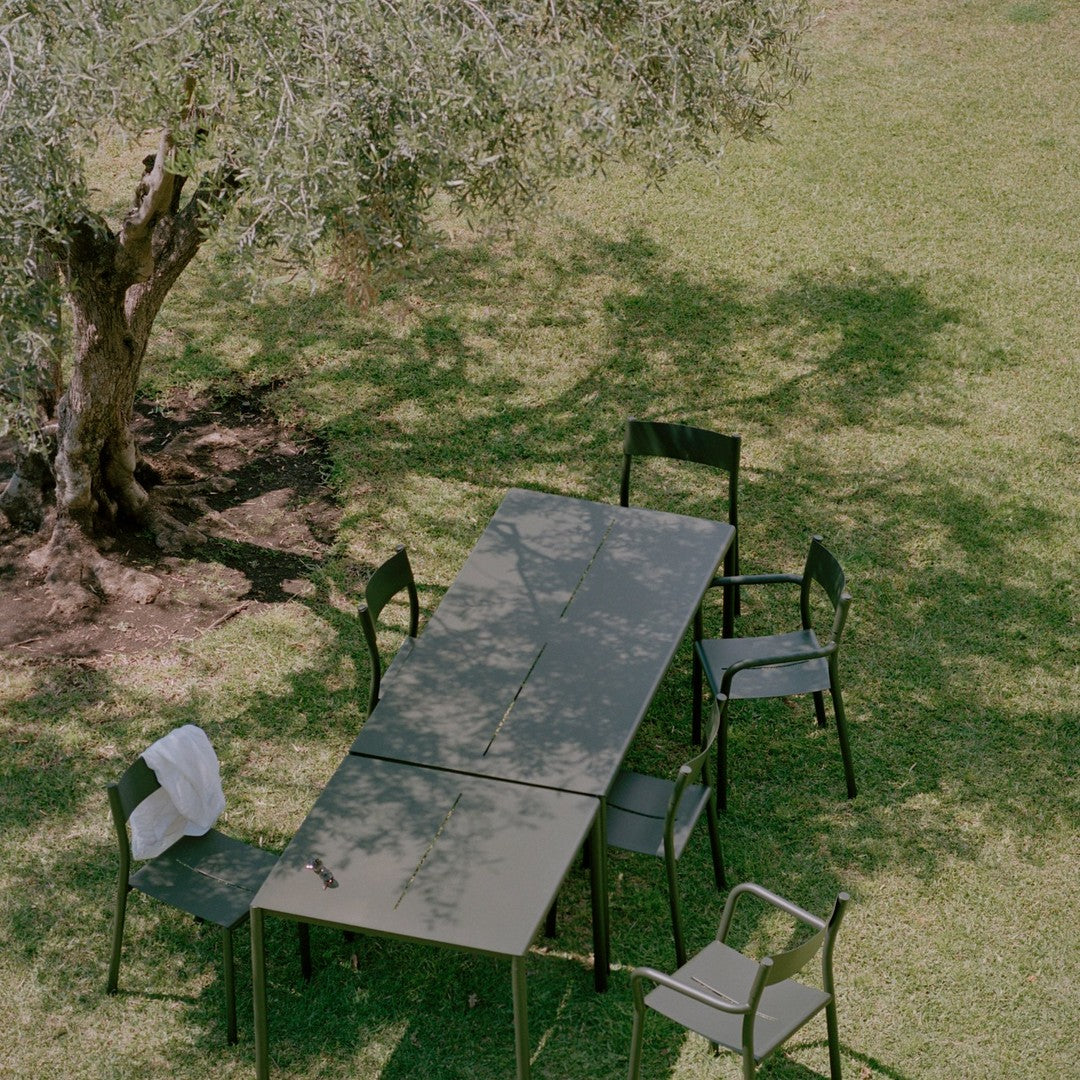 Stylish green outdoor dining set featuring a sleek grey table and minimalist black chairs against a lush grass backdrop.