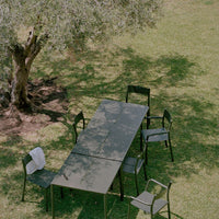 Stylish green outdoor dining set featuring a sleek grey table and minimalist black chairs against a lush grass backdrop.