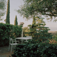 "Neutral white patio table and chairs surrounded by lush green foliage and tall evergreen trees."
