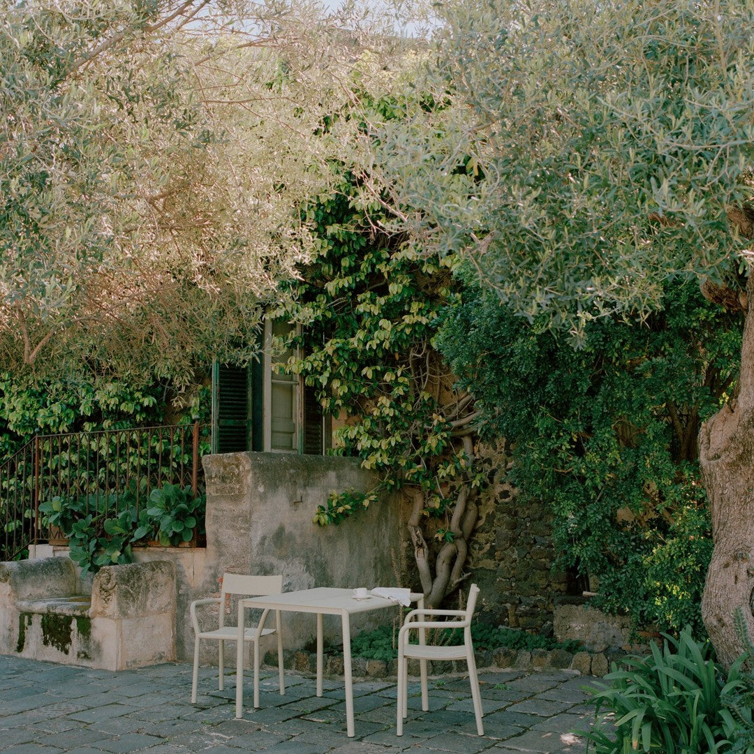 "White patio furniture against lush green foliage and rustic stone, creating a serene outdoor setting."