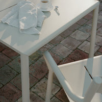 Stylish white modern table and chair set on a rustic brick pattern background, featuring soft shadows and textures.