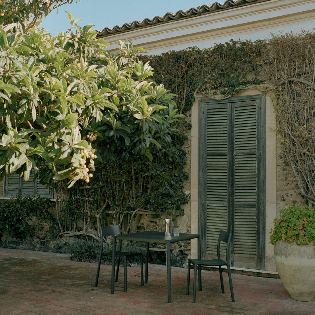 "Stylish black outdoor table and chairs against a backdrop of green foliage and textured stone wall."