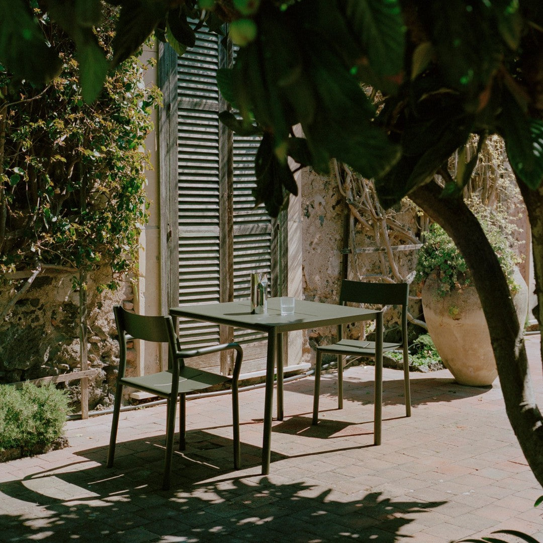 "Stylish outdoor dining set featuring muted greens and earth tones, complemented by natural sunlight and shade."