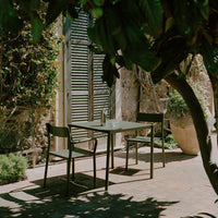 "Stylish outdoor dining set featuring muted greens and earth tones, complemented by natural sunlight and shade."