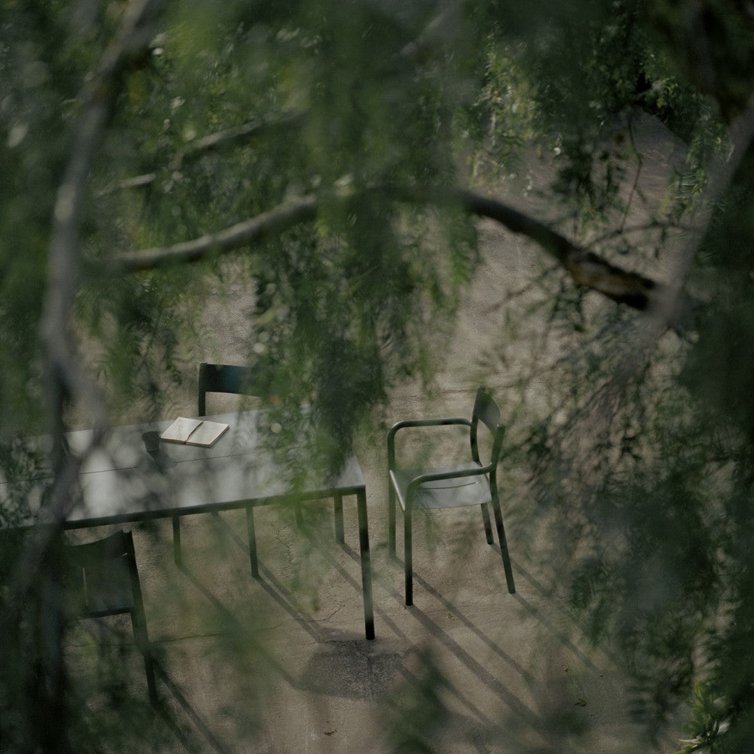 "Minimalist green metal chairs and table set against a soft, natural backdrop of leaves and earthy tones."