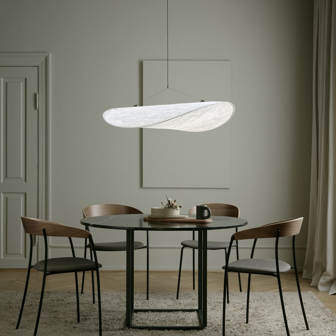 Modern white pendant light above a round black table, complemented by wooden chairs and neutral-toned decor.