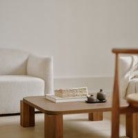 Light beige armchairs, natural wood coffee table, textured book, dark clay teapots on a neutral background.