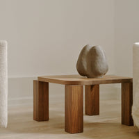 "Natural wood coffee table with soft earth tones and a minimalist design, featuring a textured gray sculpture."