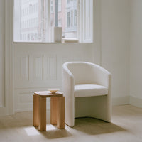 Elegant white upholstered chair with embossed pattern beside a natural wood side table in a bright room setting.