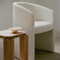 White textured armchair with intricate patterns, paired with a light wooden side table and a pale bowl.