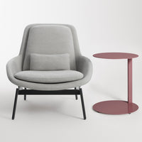 Gray upholstered armchair with a black base, paired with a round, maroon side table. Modern, minimalist design.