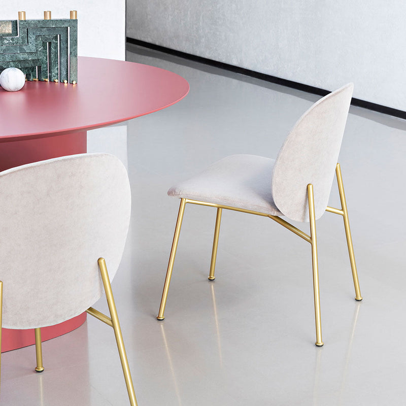 Modern beige chair with gold legs, paired with a stylish pink table in a contemporary setting.