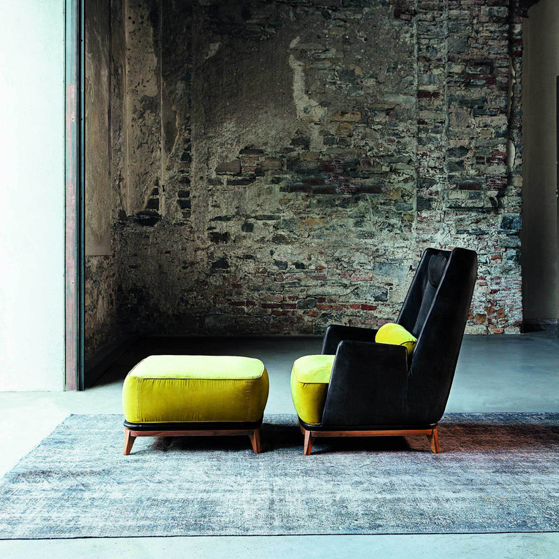 Black and yellow accent chair with matching ottoman on a textured gray rug against a rustic brick wall.