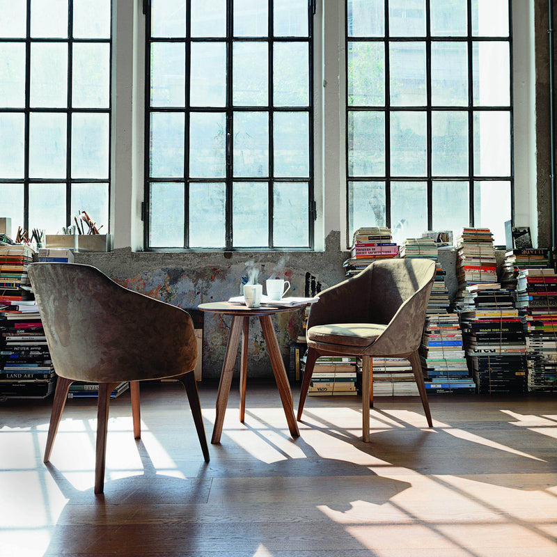 "Contemporary chairs in earthy tones, featuring soft textures, paired with a wooden table in a sunlit room."