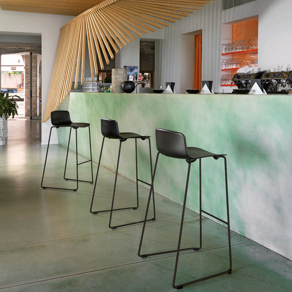 Black bar stools against a textured green and white gradient bar surface, featuring minimalist design elements.