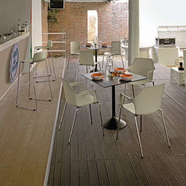 Modern outdoor space featuring white chairs and black tables against a rustic brick backdrop and wooden flooring.