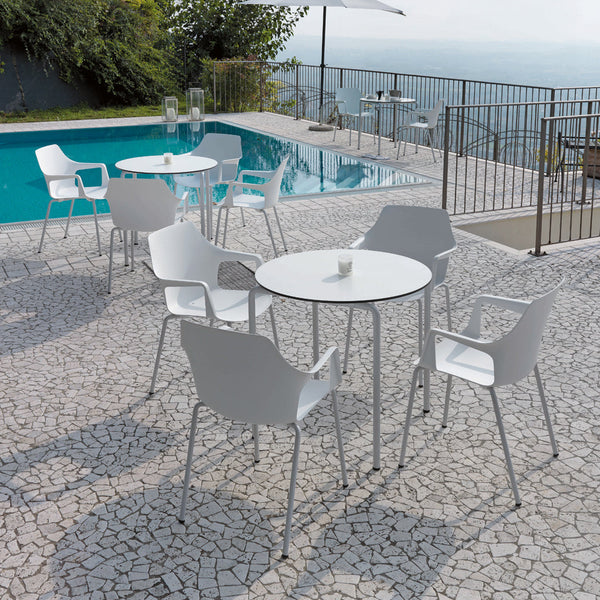 White outdoor furniture set with a round table and minimalist chairs against a mosaic stone patio by a pool.