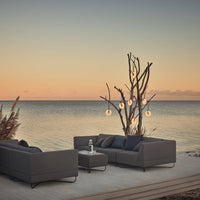 Sleek gray outdoor sofa set with subtle patterns, complemented by a serene sunset and natural accents.