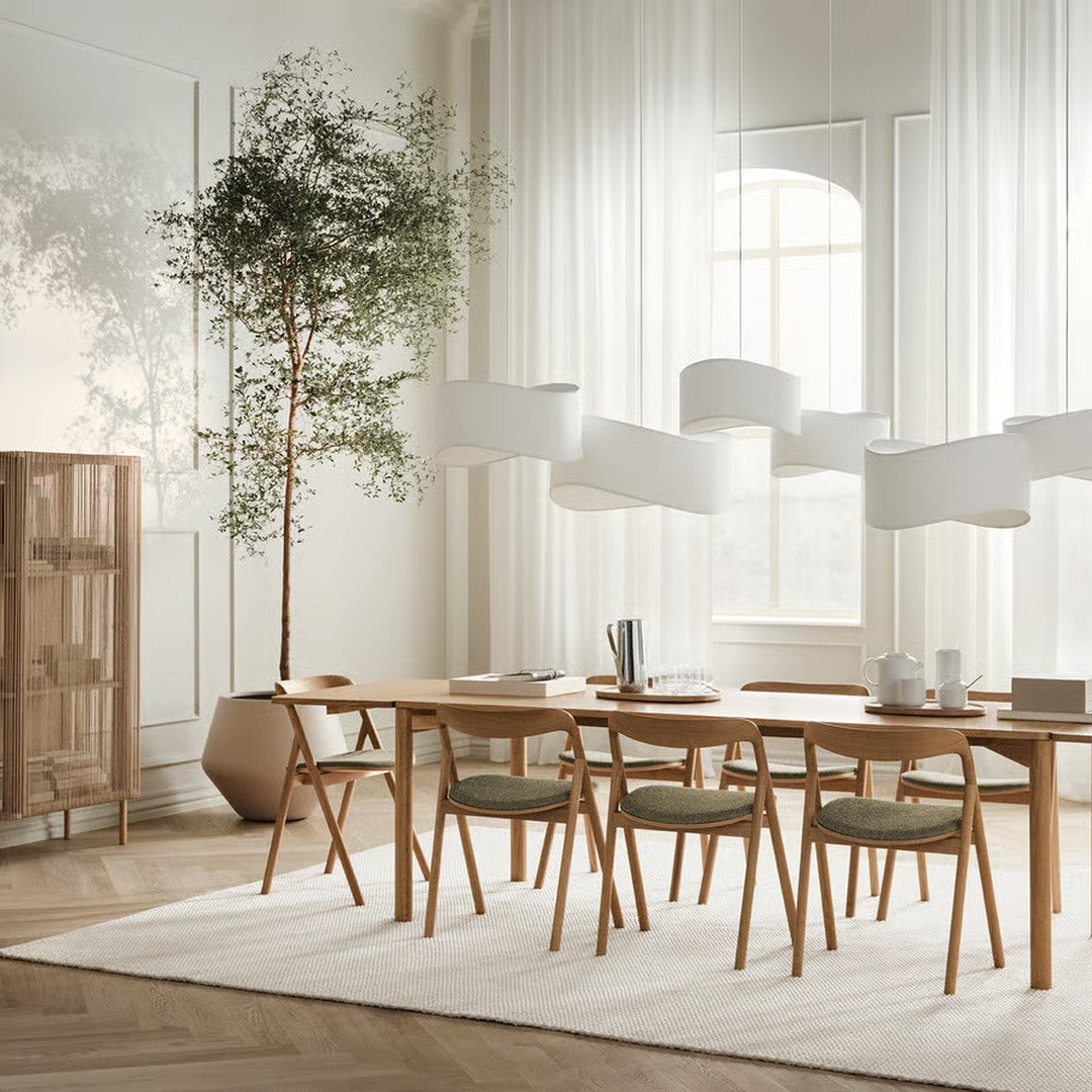 Modern dining room featuring light wood furniture, soft green cushions, and white accents surrounded by natural light.