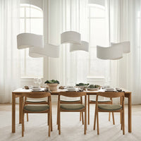 Modern wooden dining table with green upholstered chairs, surrounded by elegant white pendant lights and soft neutral decor.