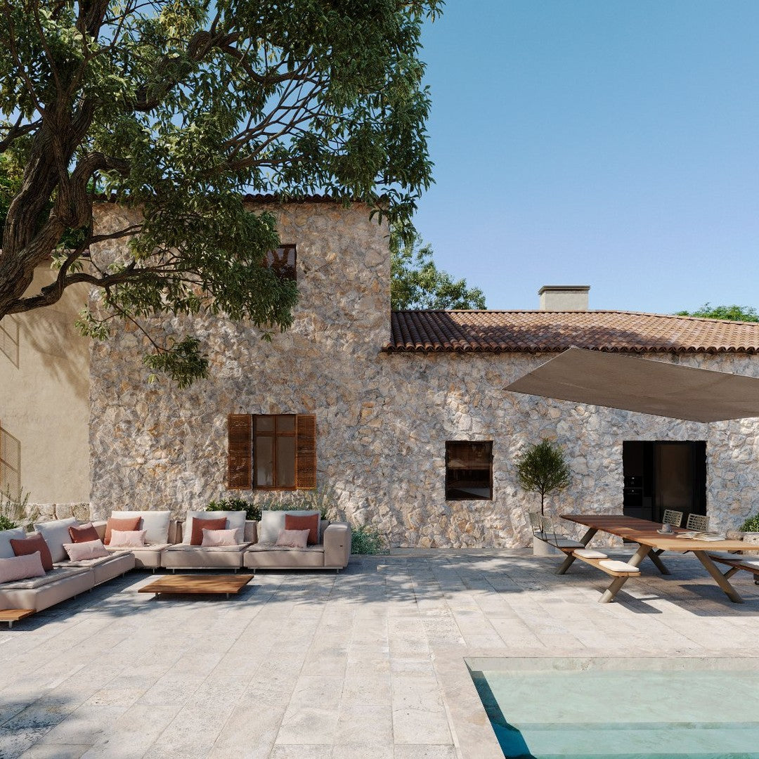 "Textured stone wall, warm terracotta roof, soft beige sofa with earthy cushion colors, clear blue sky backdrop."