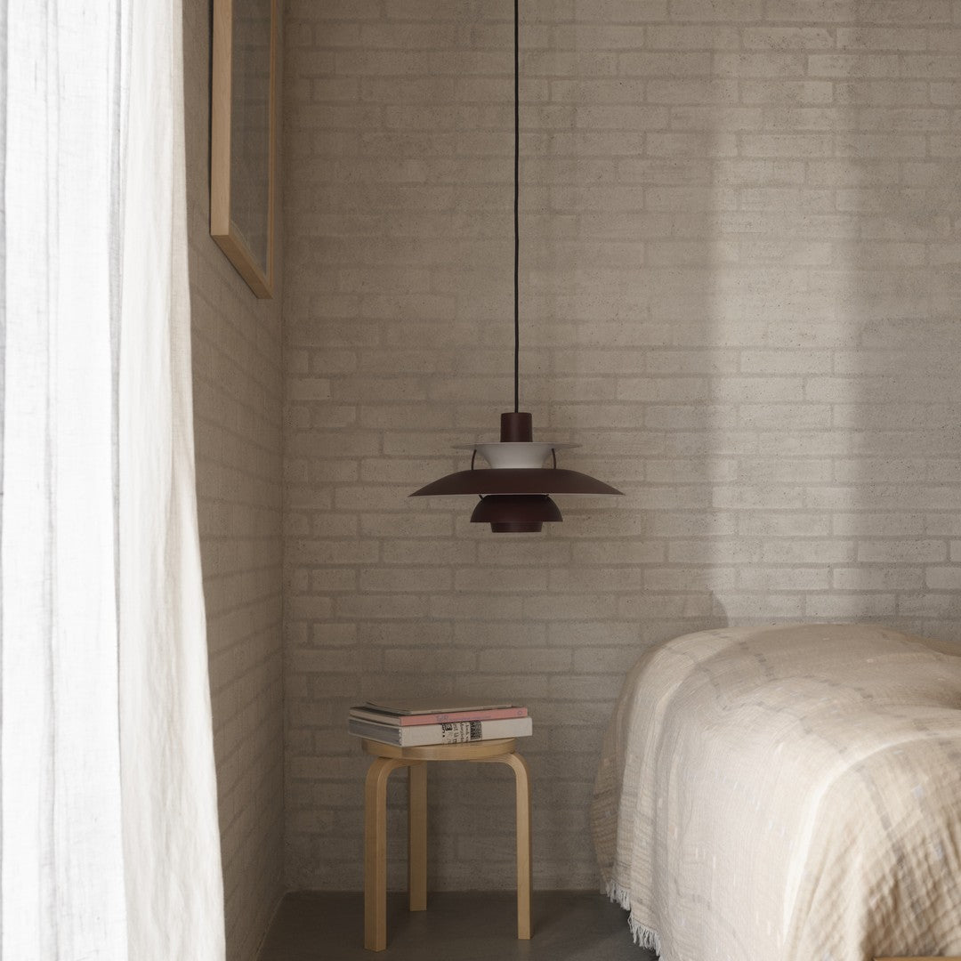 "Modern pendant lamp in deep maroon, white, and brass accents, with a sleek, minimalist design against a textured backdrop."