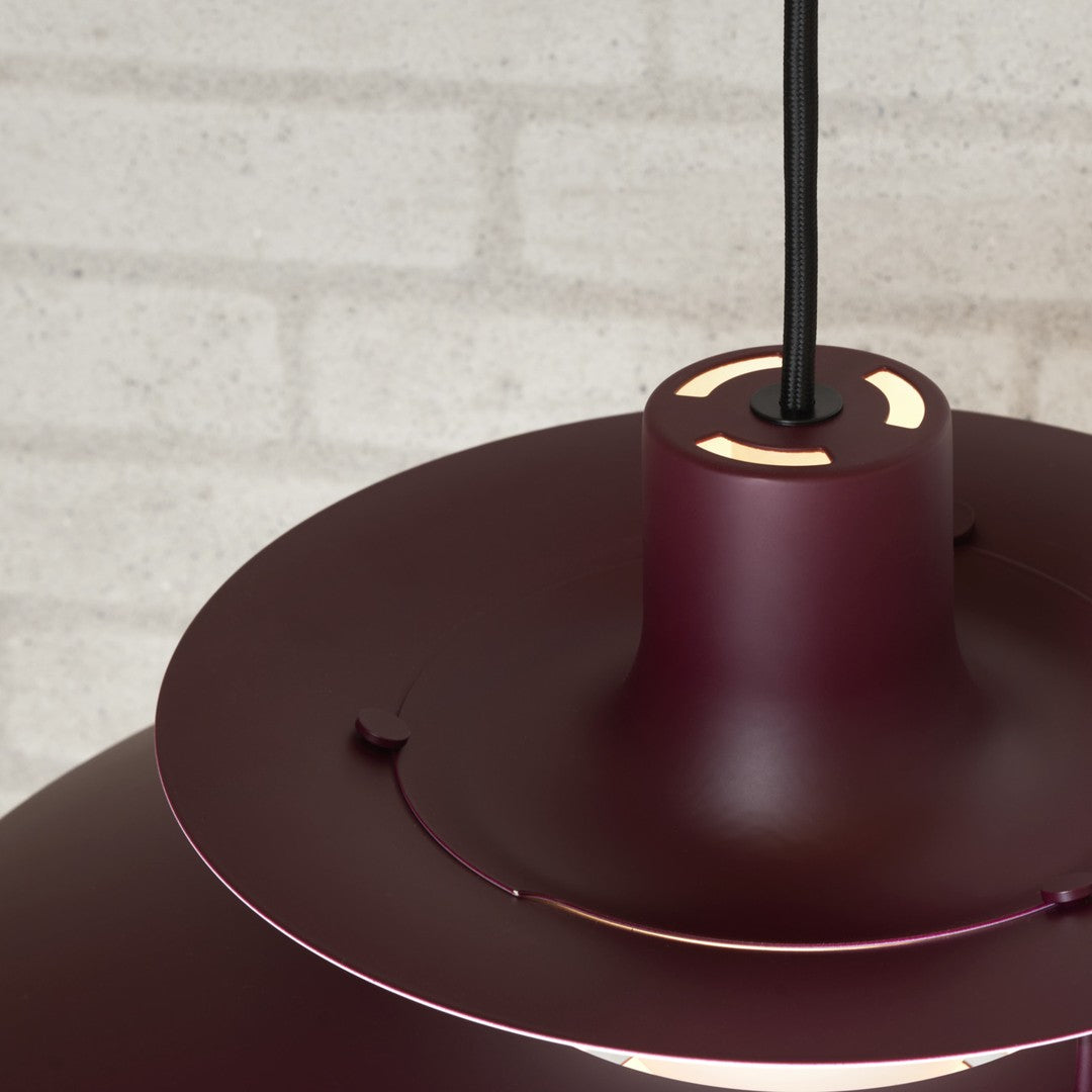 Burgundy pendant lamp with sleek metallic accents and a minimalist design against a textured gray wall.
