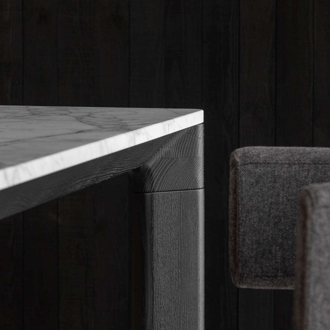 "Gray marble table edge with a sleek black wooden base and dark gray upholstered chair against a black wood backdrop."