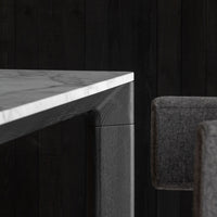 "Gray marble table edge with a sleek black wooden base and dark gray upholstered chair against a black wood backdrop."