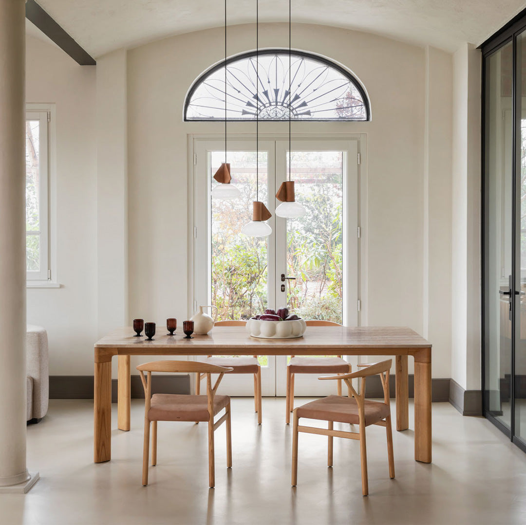 Elegant wooden dining table with soft beige chairs, featuring neutral tones and geometric light fixtures.