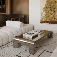 Modern silver coffee table on textured white rug, with soft beige sectional and vibrant wall art in a cozy living room.