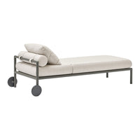 Light beige daybed with rolled cushions and dark gray metal frame; sleek, minimalist design, perfect for modern decor.