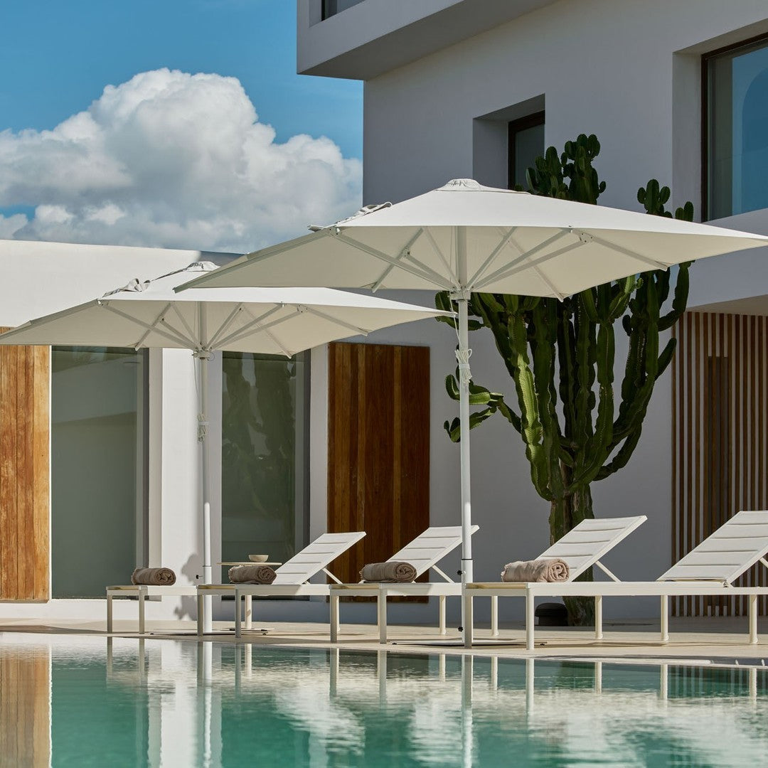 White umbrellas beside a turquoise pool, with a backdrop of beige walls and green cacti. Perfect for outdoor relaxation.