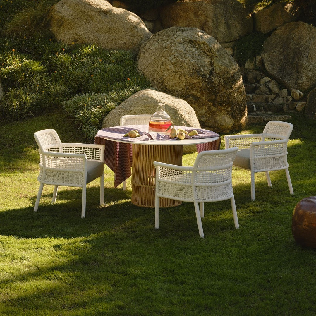 White outdoor chairs surround a round table with a vibrant purple tablecloth, set on lush green grass.
