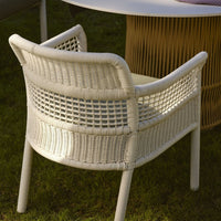 White woven chair with a textured pattern, set against a natural green grass backdrop.