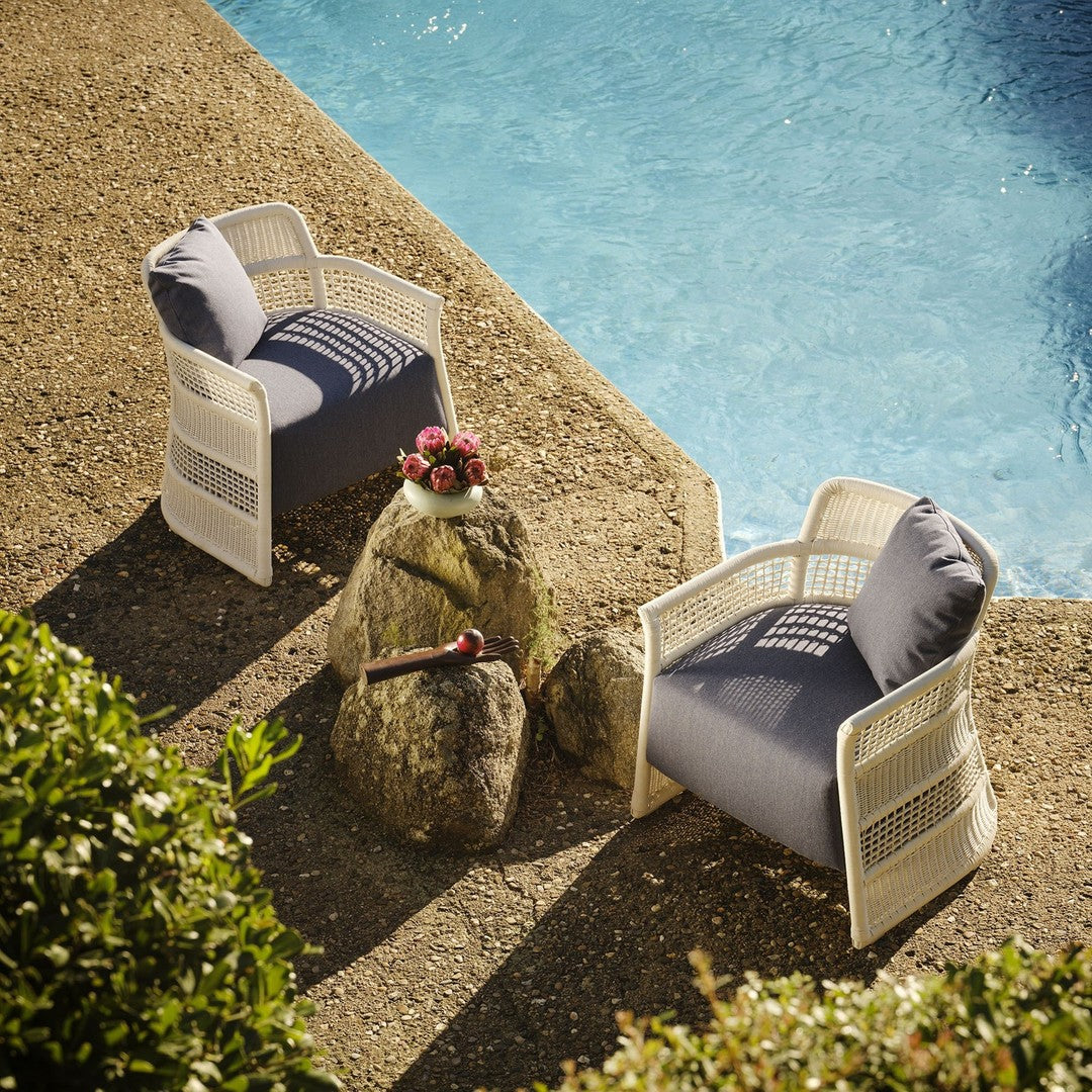 Two white outdoor chairs with navy striped cushions, set beside a pool, surrounded by greenery and a natural stone table.