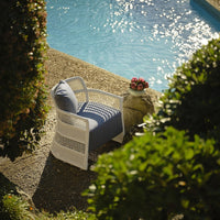 Blue cushioned chair with white woven frame, set beside a shimmering pool amidst lush greenery.