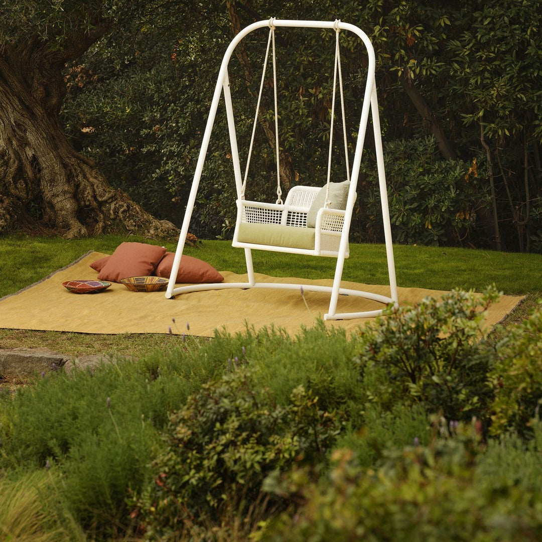 White swing chair with a sleek design, surrounded by green grass and earth-toned cushions on a golden mat.