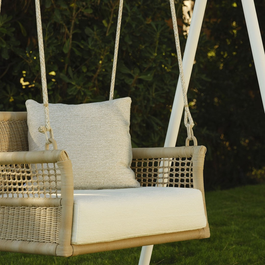 Neutral tones with woven texture and a cozy, light gray pillow on a white swing seat against lush green grass.
