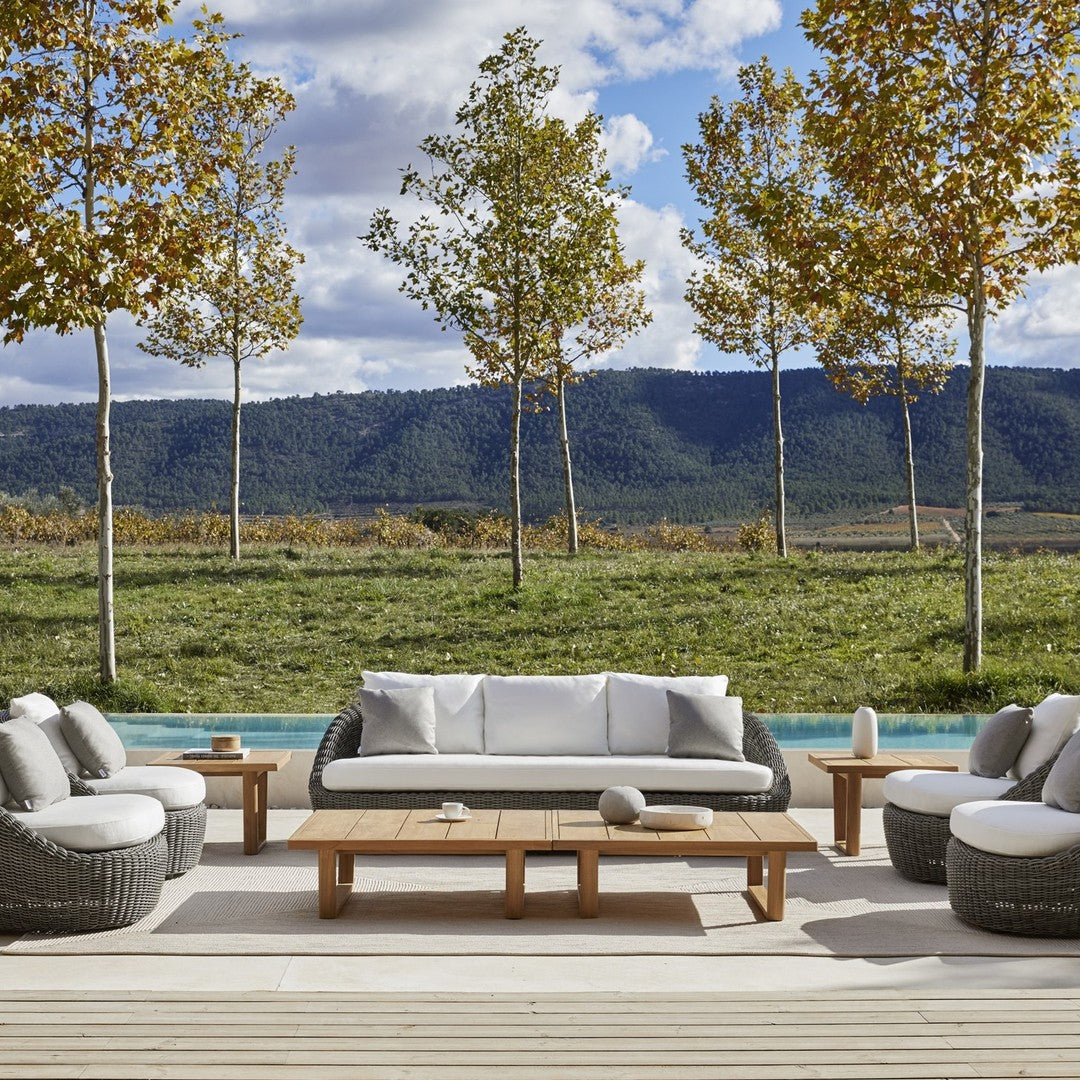"Cozy outdoor seating set featuring gray cushions and natural wood accents, surrounded by lush greenery and autumn trees."