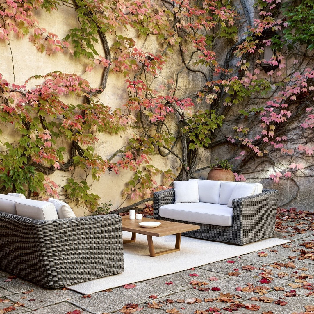 Gray wicker outdoor seating with white cushions, set against a backdrop of pink and green ivy leaves in autumn.