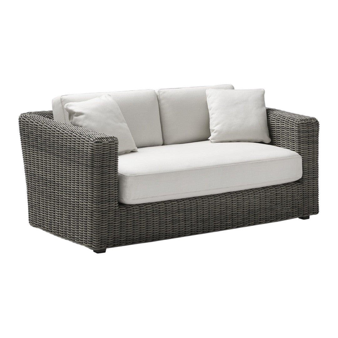 Gray wicker loveseat with light beige cushions and two matching pillows, perfect for outdoor or indoor decor.