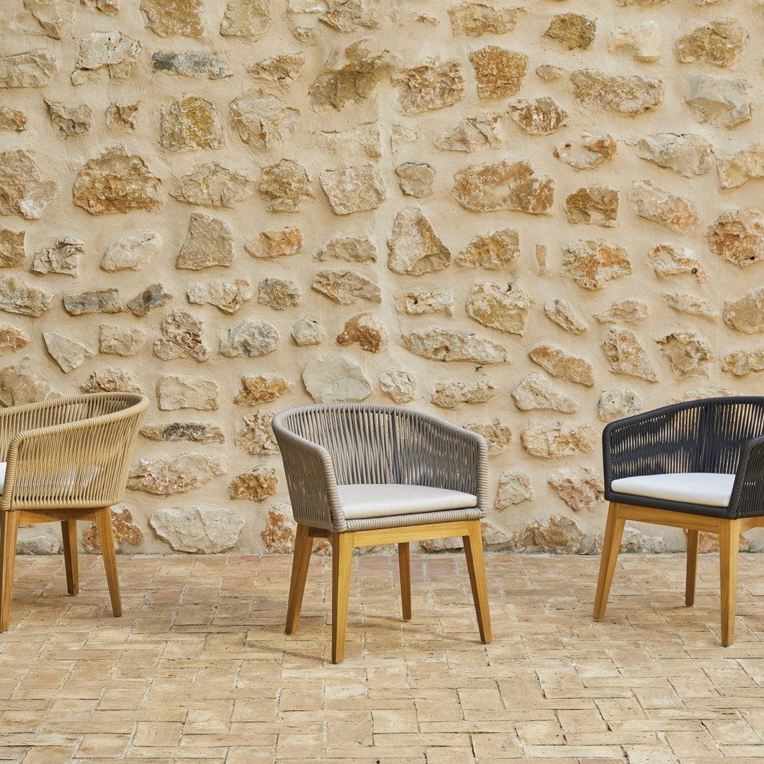 Three stylish chairs in natural, gray, and dark blue woven patterns against a textured stone wall.