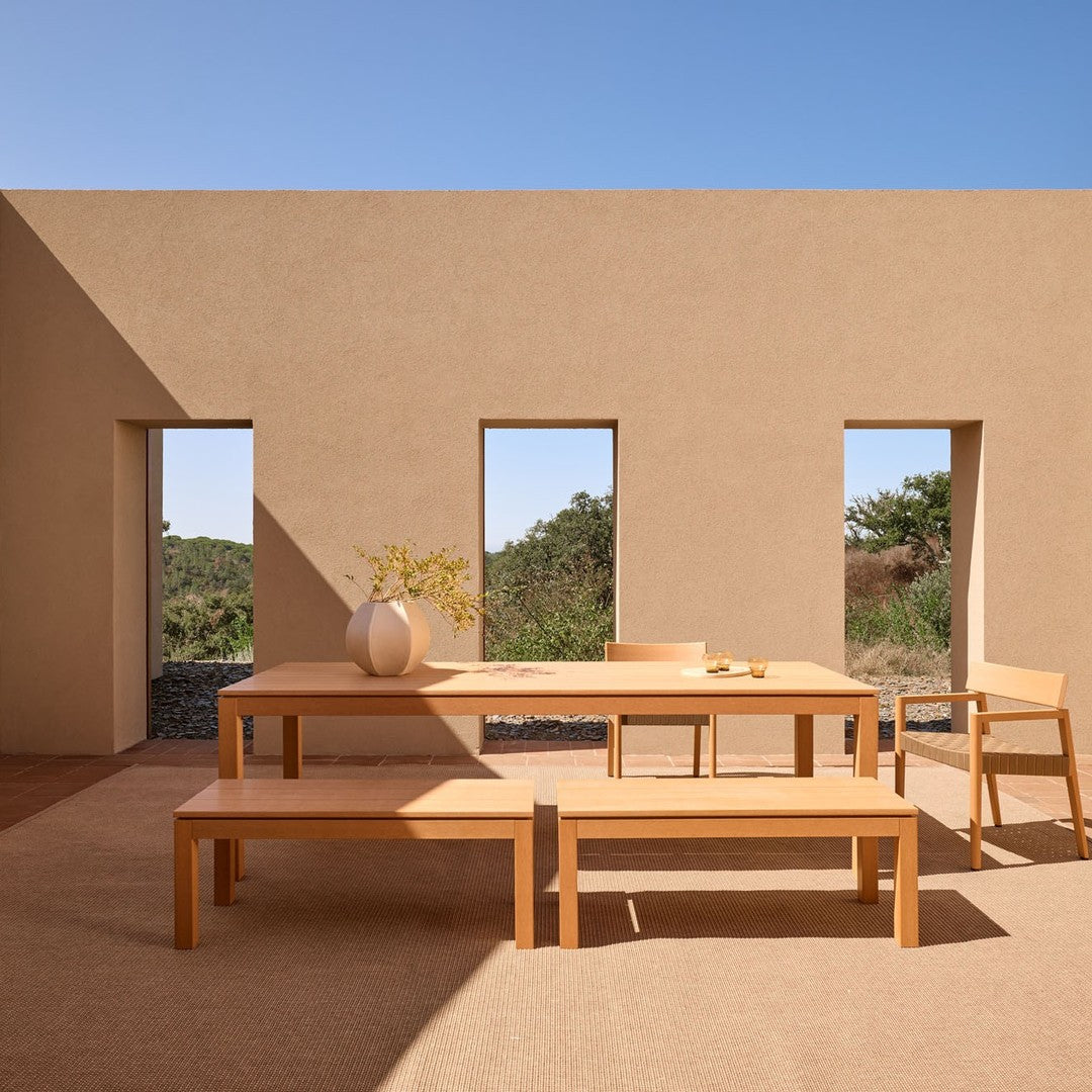 Light wood dining set with a minimalist design, set against earthy-toned walls and a clear blue sky.
