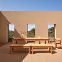 Light wood dining table and benches against a warm, neutral-toned wall with natural light and minimalistic design.