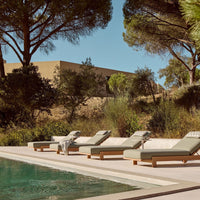 "Light grey lounge chairs with subtle patterned cushions beside a tranquil blue pool surrounded by lush greenery."